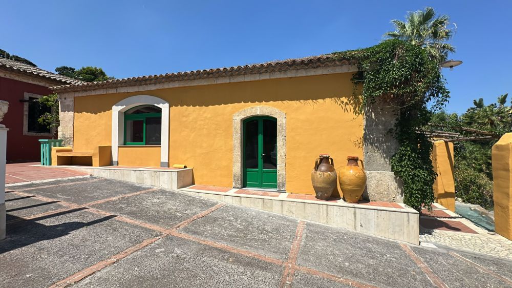 Facciata di fabbricato rurale ocra con infissi verdi, portale in pietra e giare tradizionali.