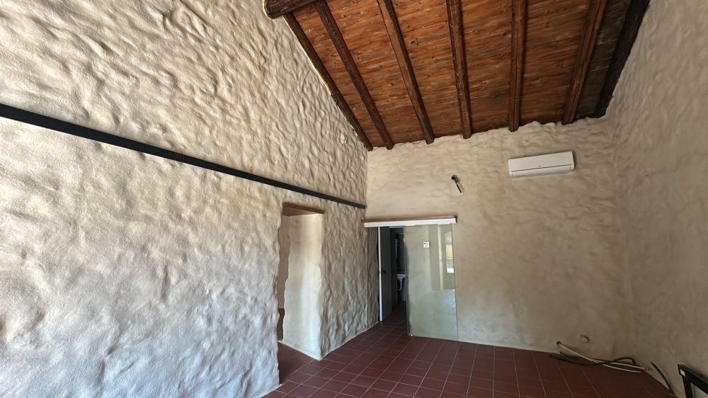 Ambiente interno ristrutturato con pavimento in cotto, pareti chiare e soffitto in travi di legno