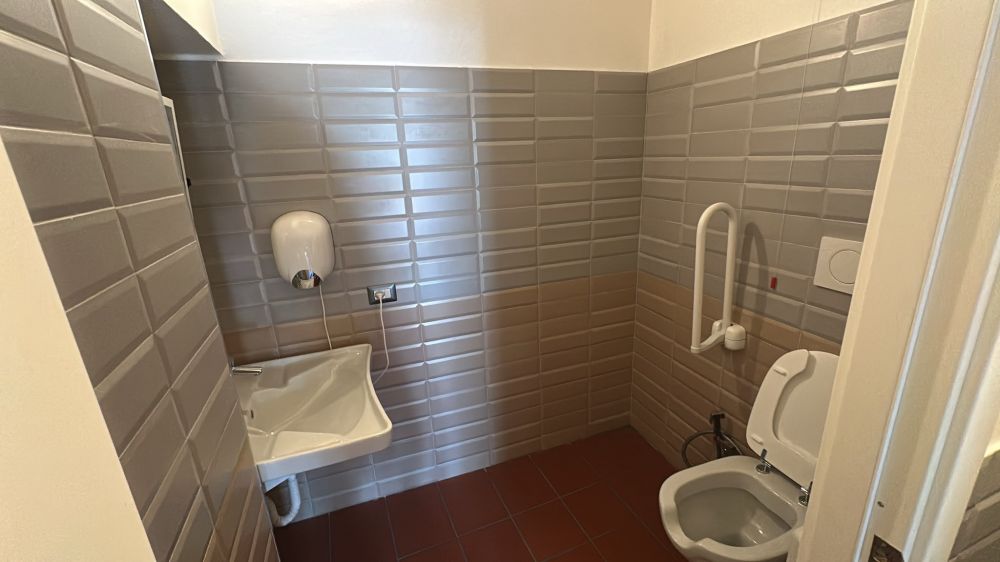 Bagno accessibile a disabili sensoriali e motori con WC con maniglione e lavabo ergonomico.